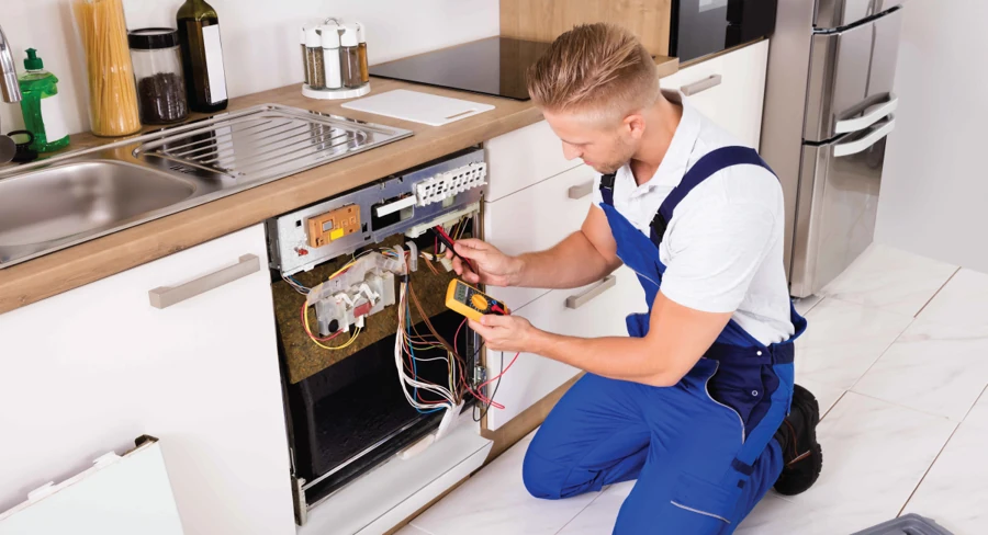 Technician testing exposed dishwasher wiring with a multimeter