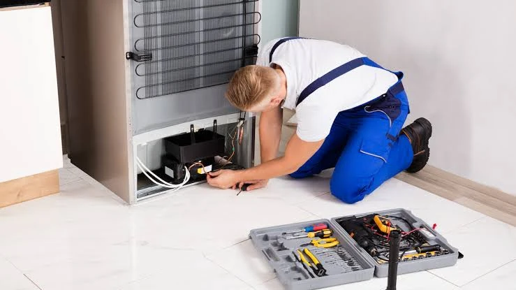 Technician checking a refrigerator compressor and rear cooling components